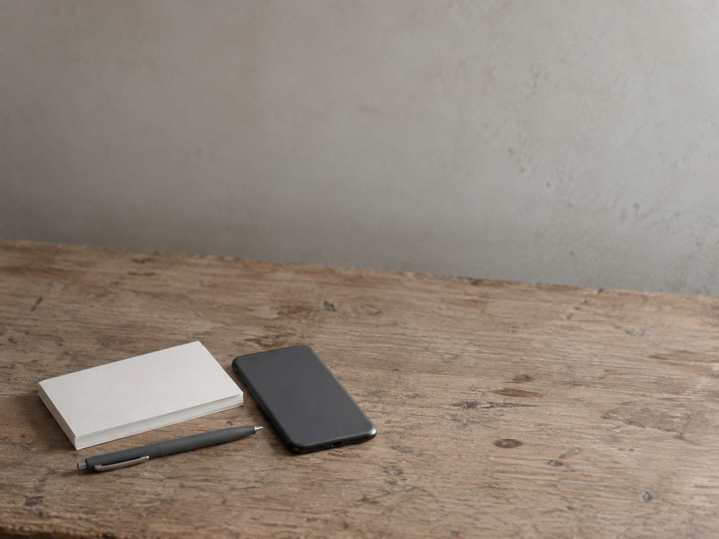 A short stack of blank postcards and a capped pen on a shop counter beside a face-down phone.