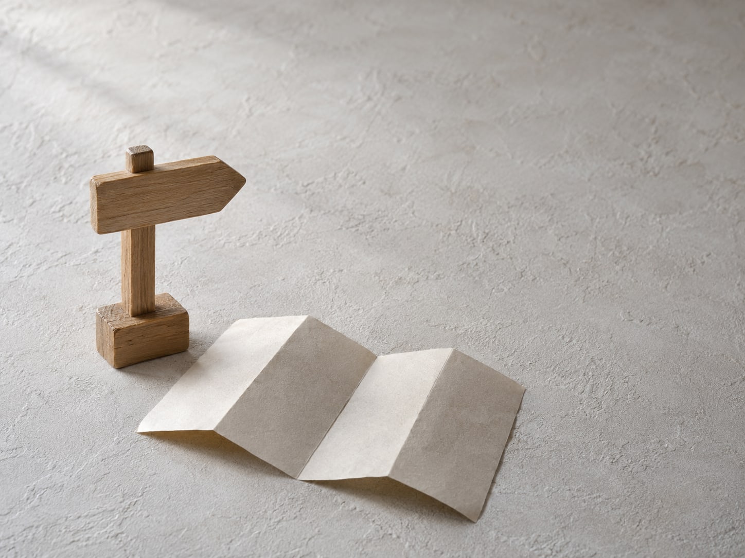 A single wooden signpost-shaped block beside a folded paper map on a plain light surface.