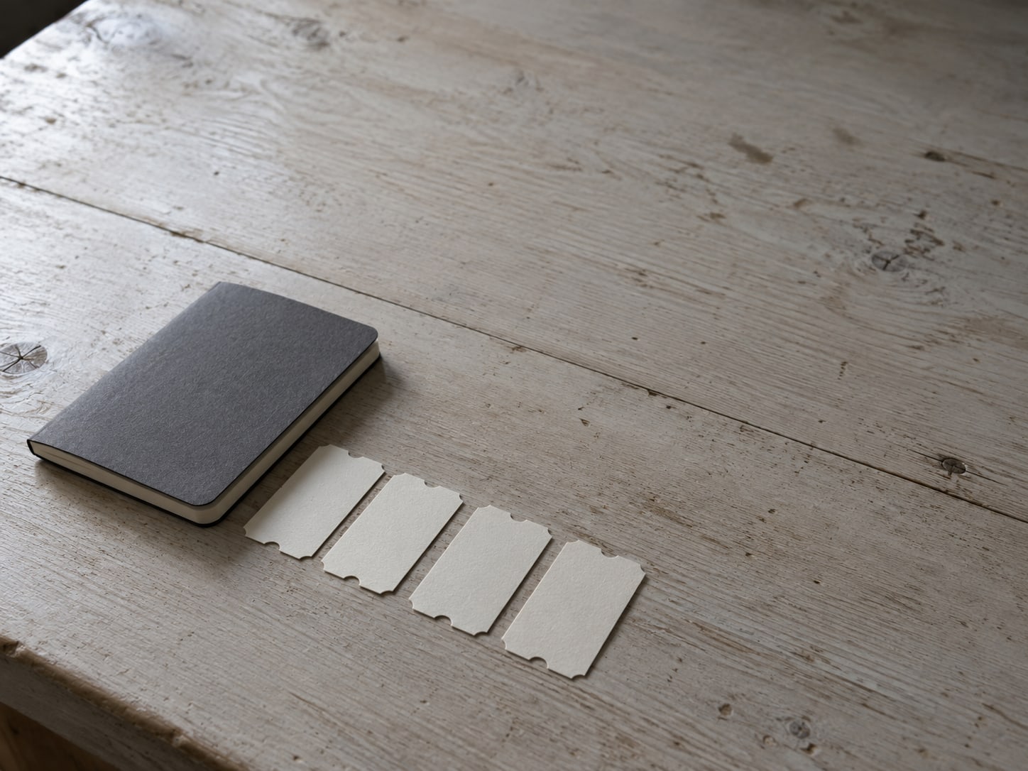 A tidy row of unmarked paper tickets and a small closed notebook lined up on a wooden counter.