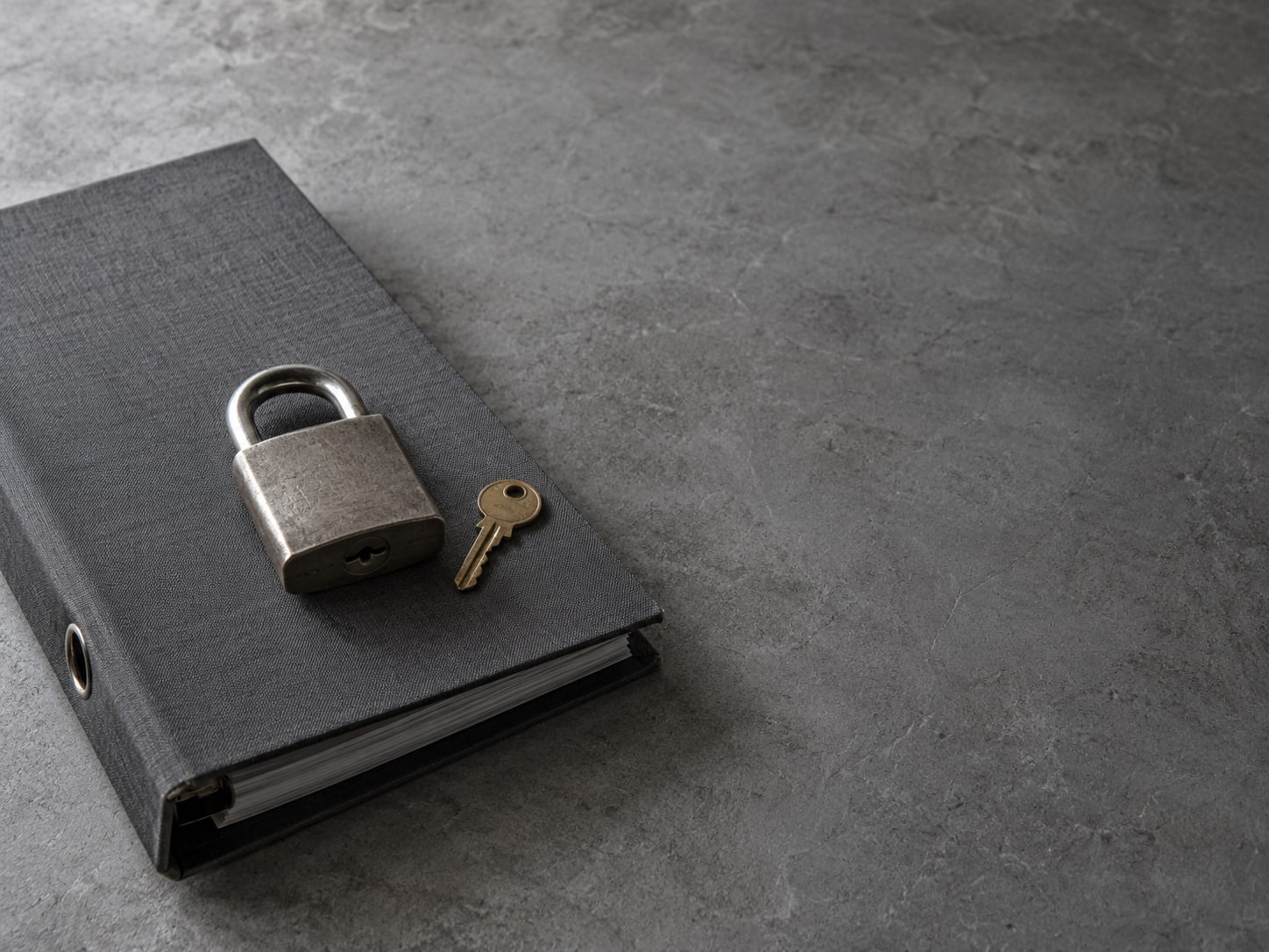 A padlock resting on a closed ring binder beside a small brass key on a gray table.