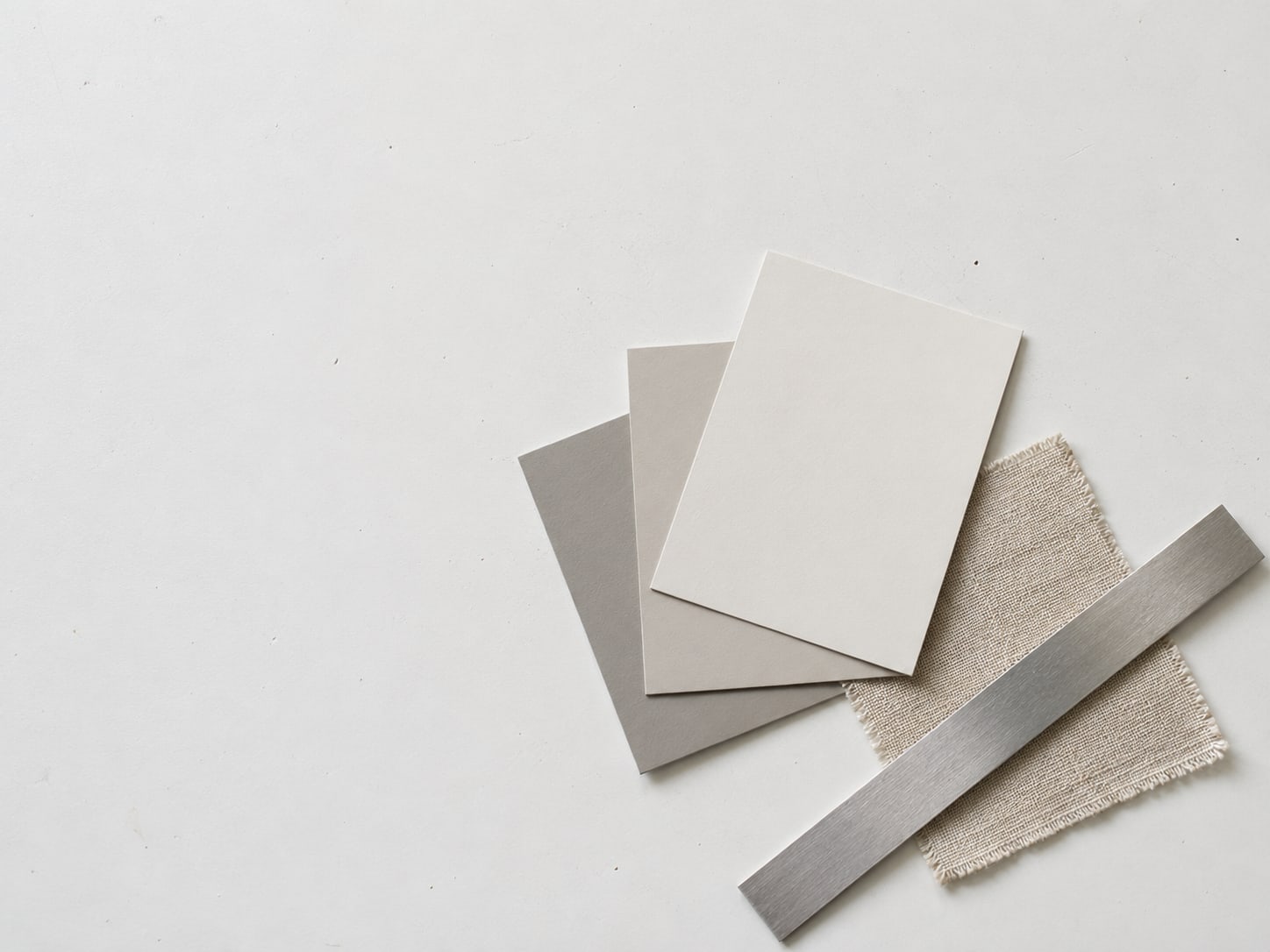 A flat arrangement of paint swatch cards, a ruler and a small fabric sample on a white table.