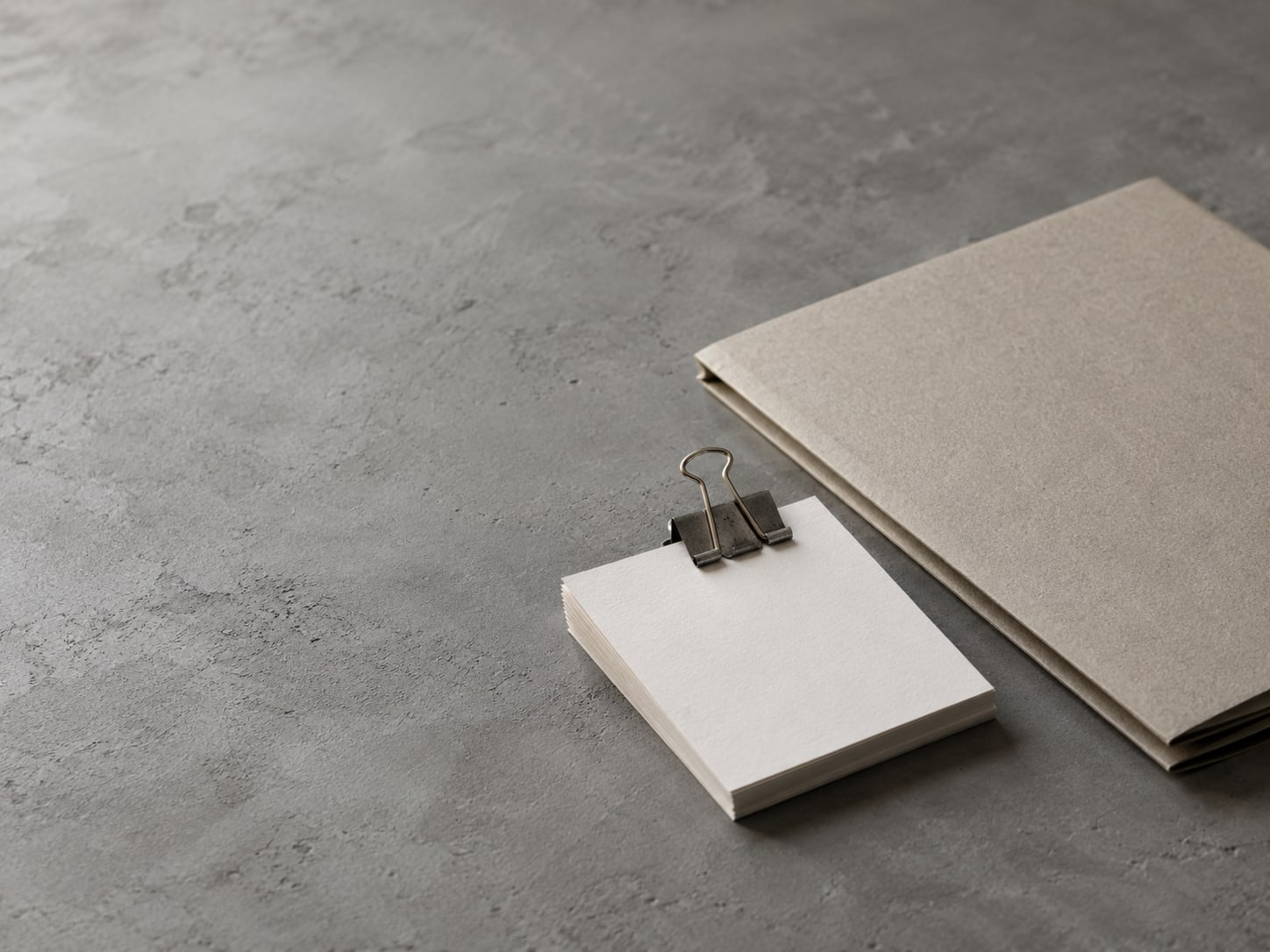 A stack of blank index cards held by a binder clip beside a closed folder on a gray surface.