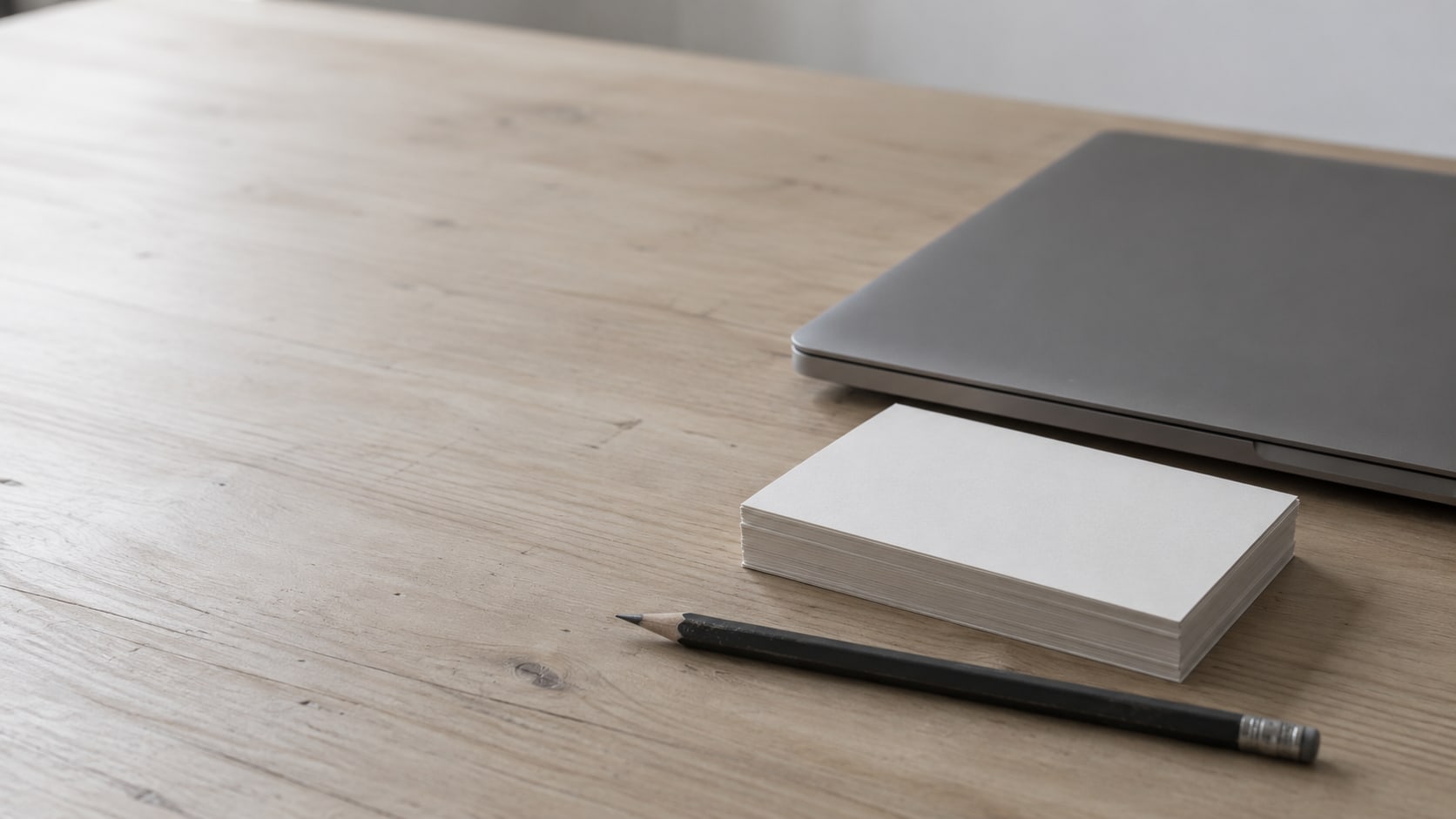 A closed laptop, a small stack of blank index cards and a pencil arranged on a clean desk.