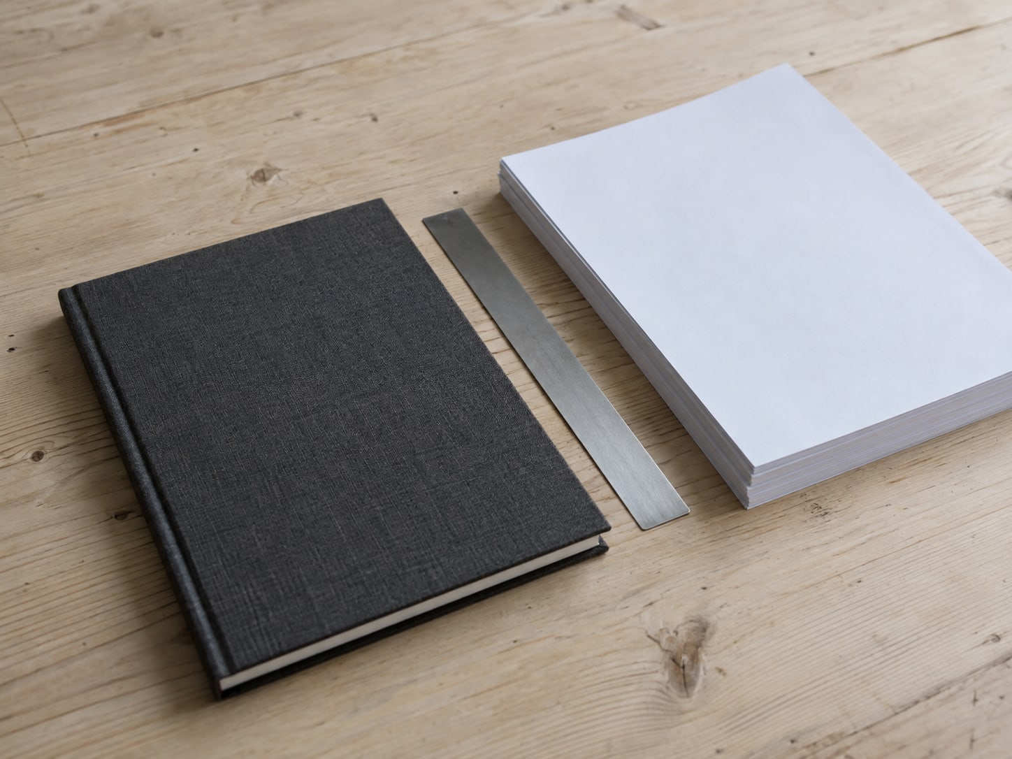 A desk with a closed notebook, a ruler and a stack of printed pages squared into a neat pile.