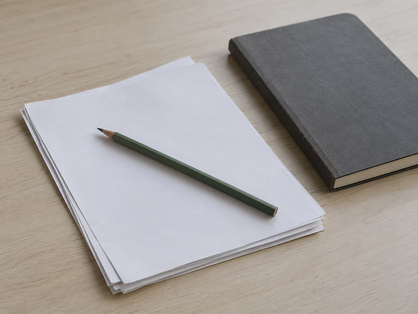 A small stack of printed pages with a green pencil laid across them next to a closed notebook.