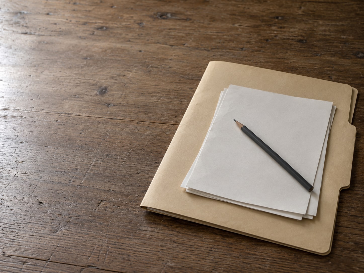A closed manila folder with a small stack of blank papers and a pencil resting on top.