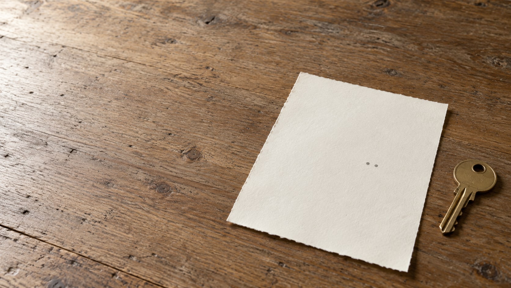 A blank sheet of paper with two small pencil dots close together and a plain brass key on a wooden counter.