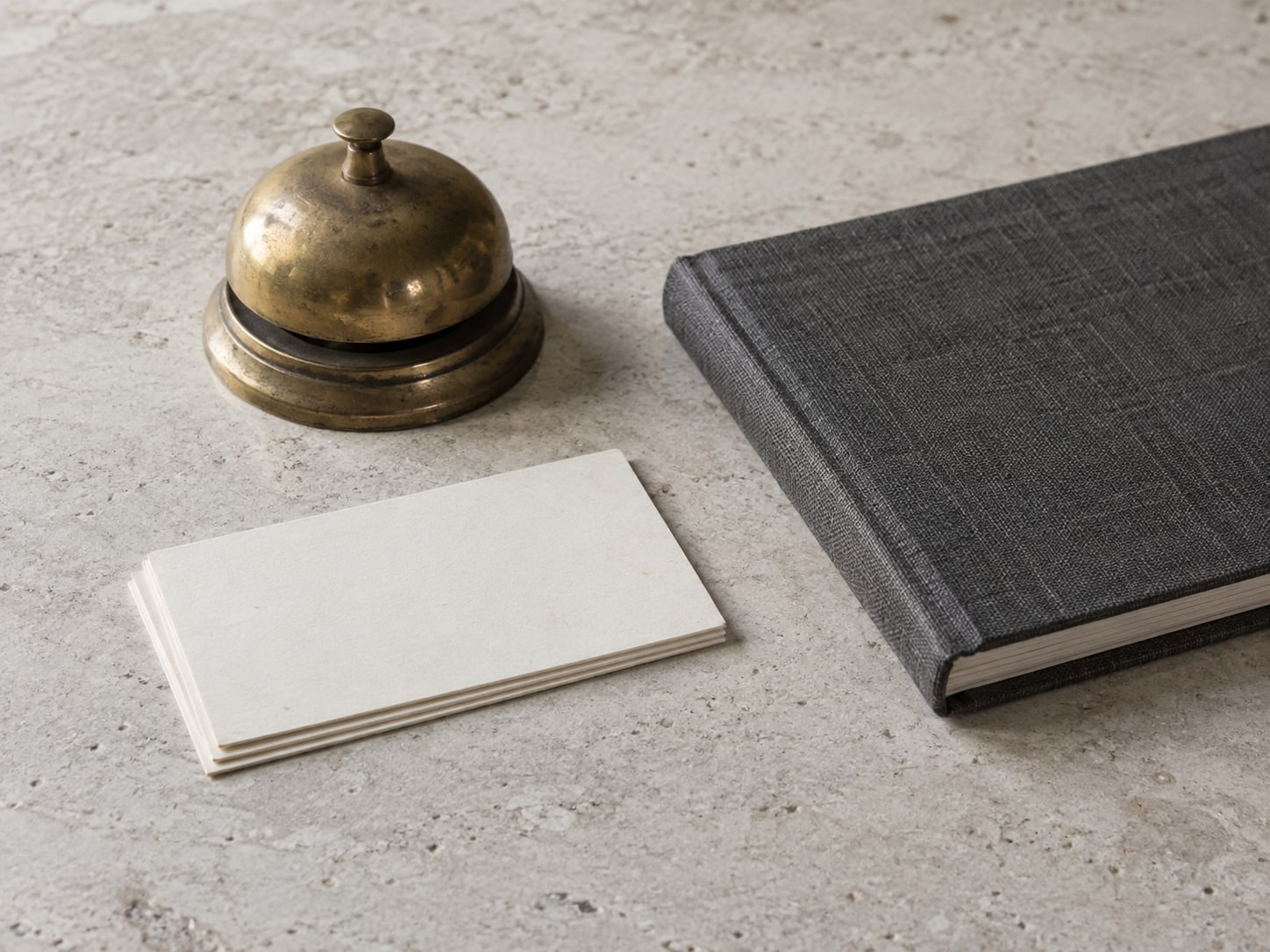 Tres fichas en blanco apiladas junto a una pequeña campana de latón y un cuaderno cerrado sobre un mostrador.