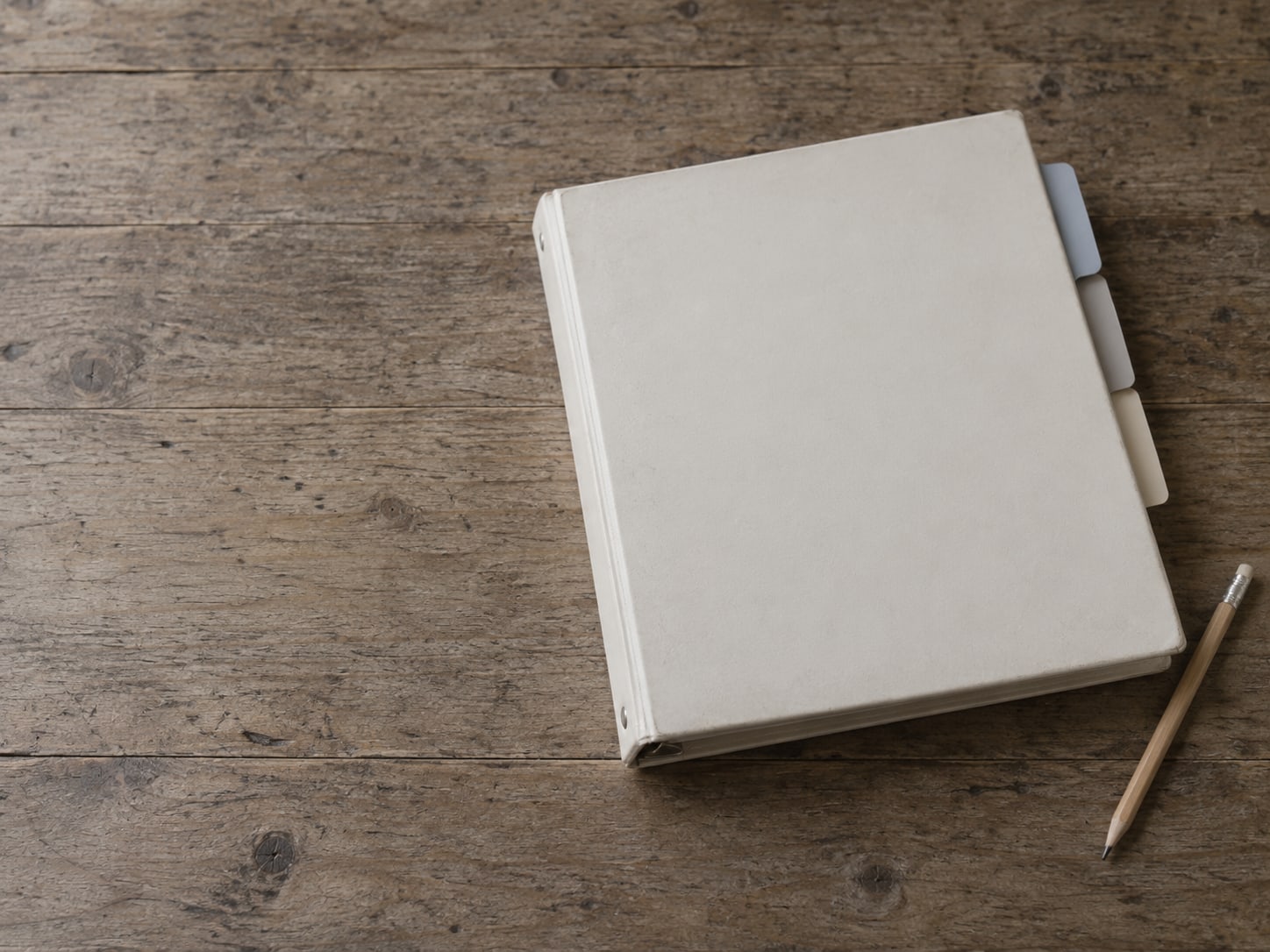 A closed three-ring binder with blank colored tab dividers beside a pencil on a desk.