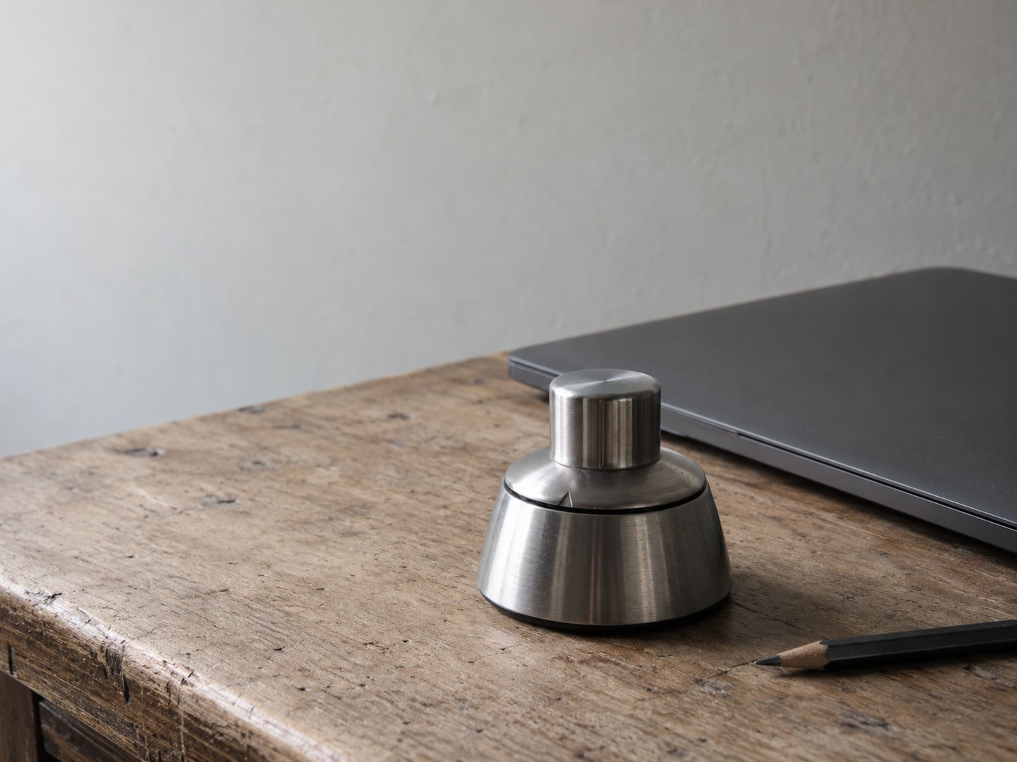 A kitchen timer set on a desk beside a closed laptop and a pencil.