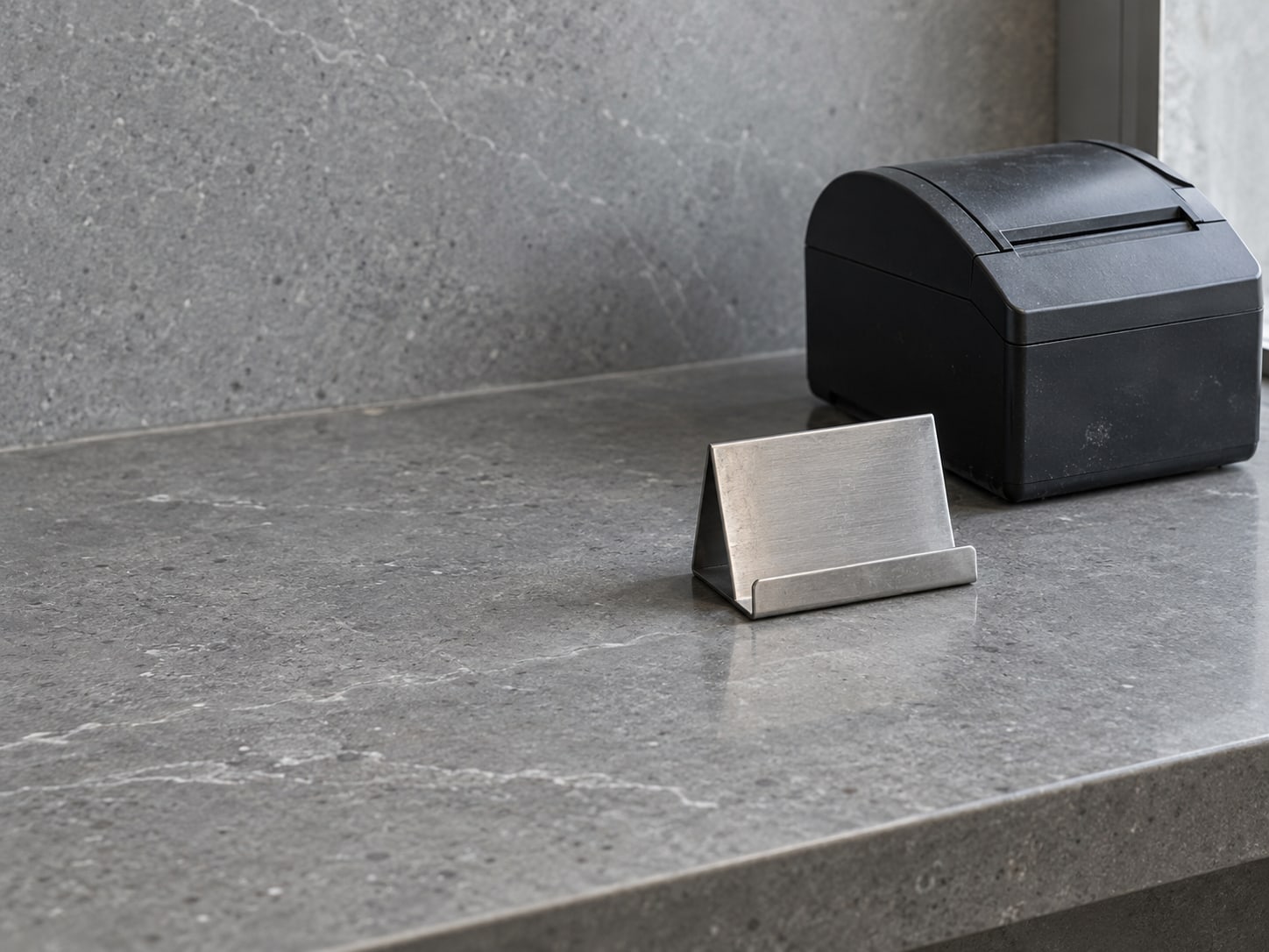 A small empty card stand on a clean service counter next to a closed receipt printer.