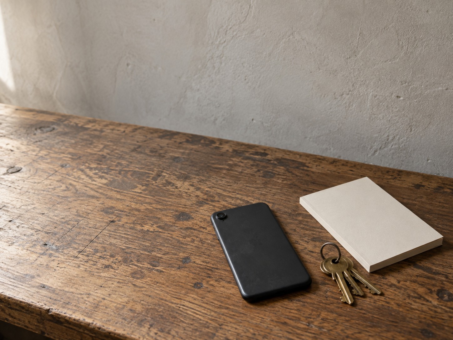 A face-down phone beside a ring of shop keys and a blank notepad on a worn wooden counter.