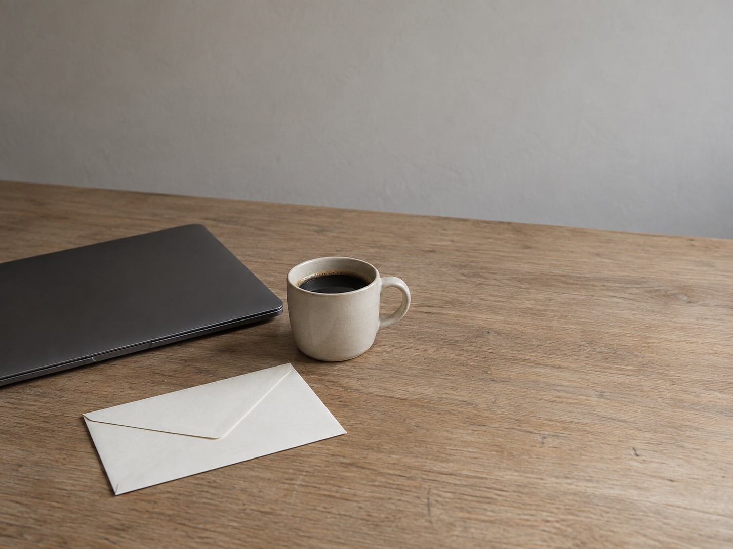 A single unopened envelope resting on a clean wooden desk beside a closed laptop and a cup of coffee.