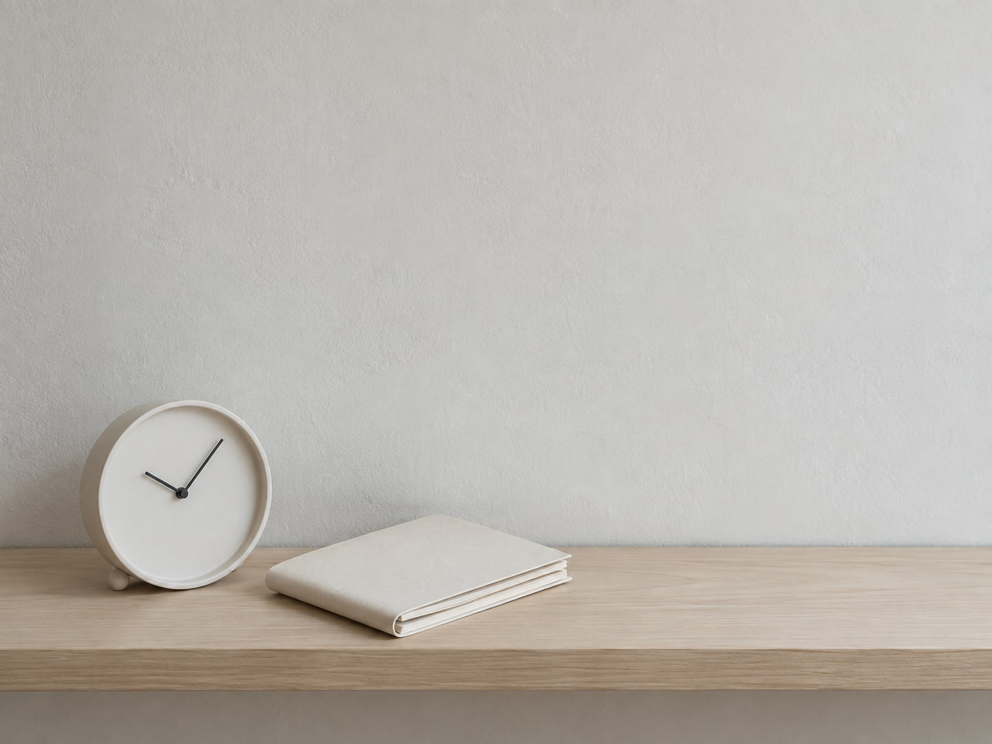 A small wall clock and a folded paper planner with blank pages on a tidy shelf.