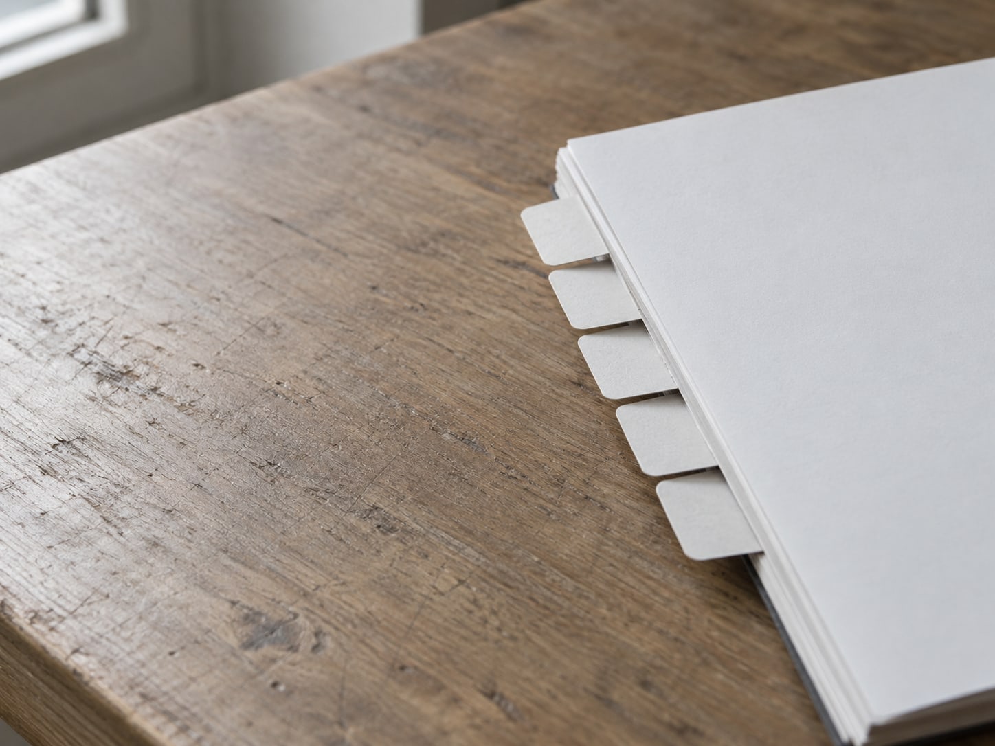 A tidy row of folded paper tabs lined up along the edge of a wooden desk beside a blank notepad.