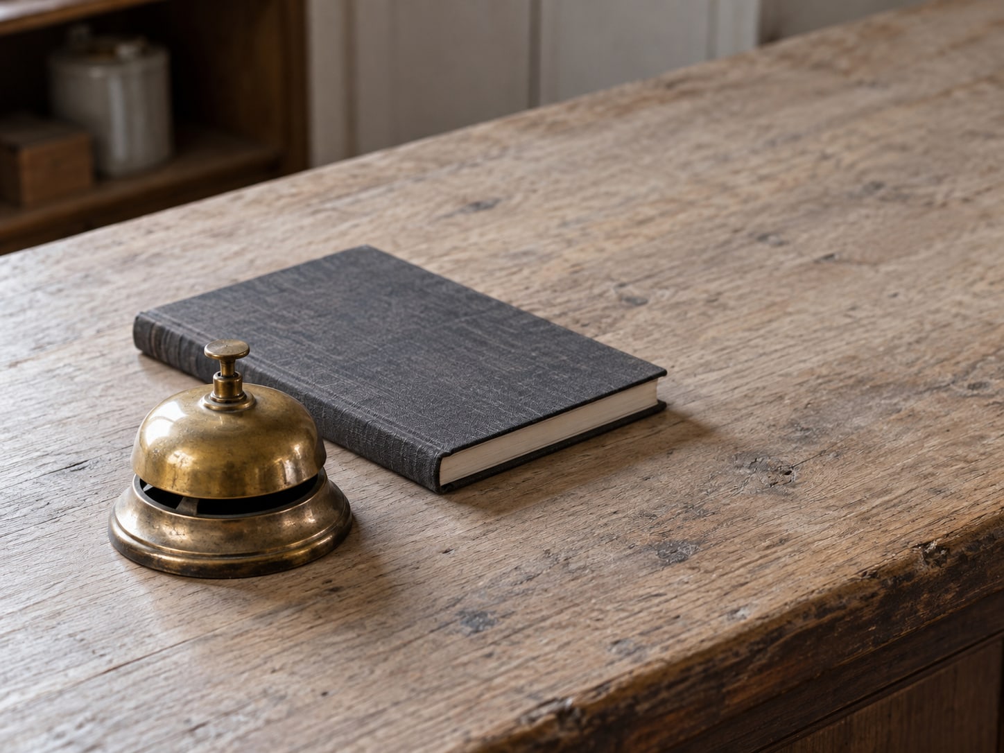 A small brass service bell on an empty wooden shop counter beside a closed appointment book.