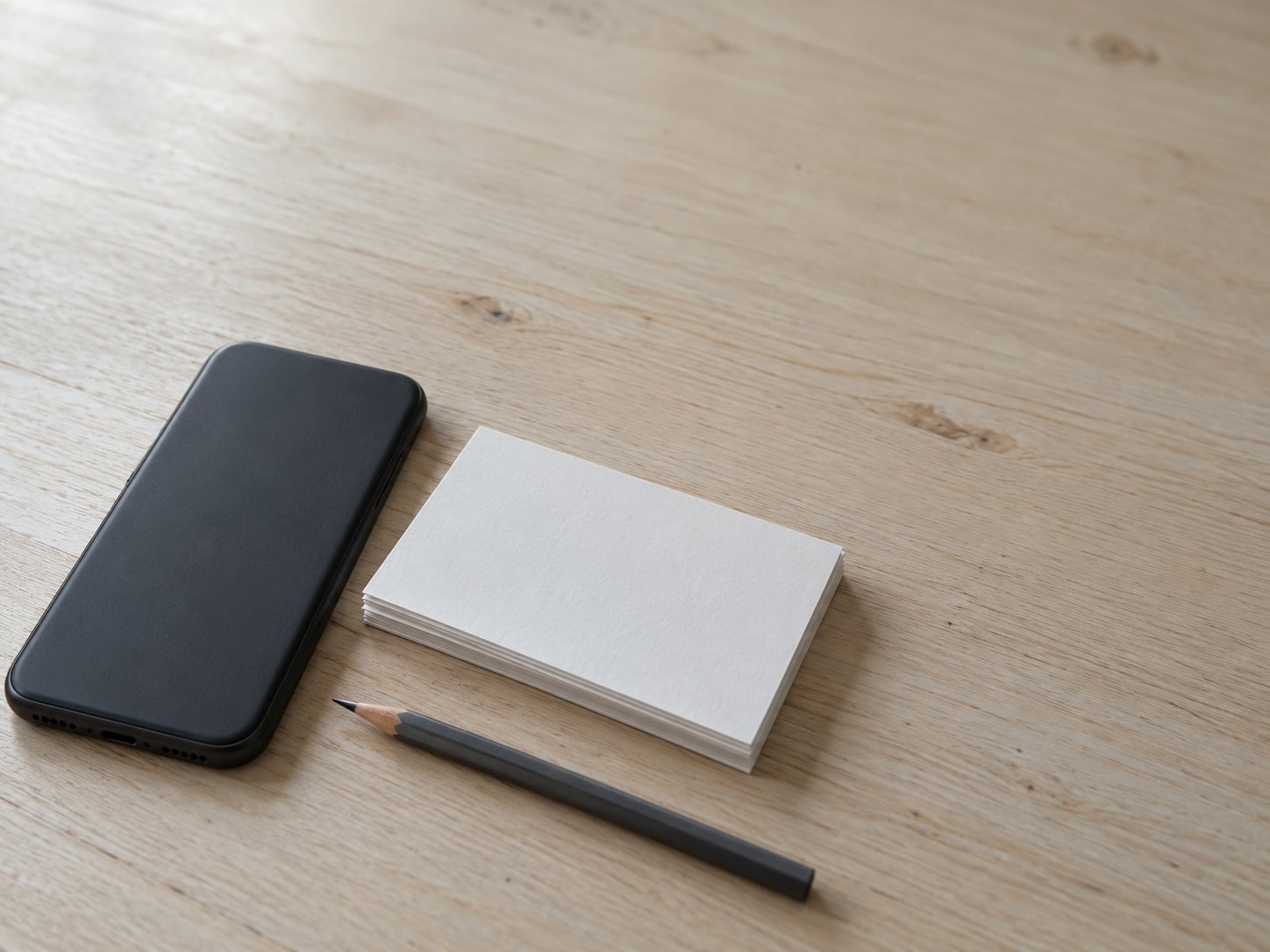 A closed phone lying face down beside a stack of blank index cards and a sharpened pencil.