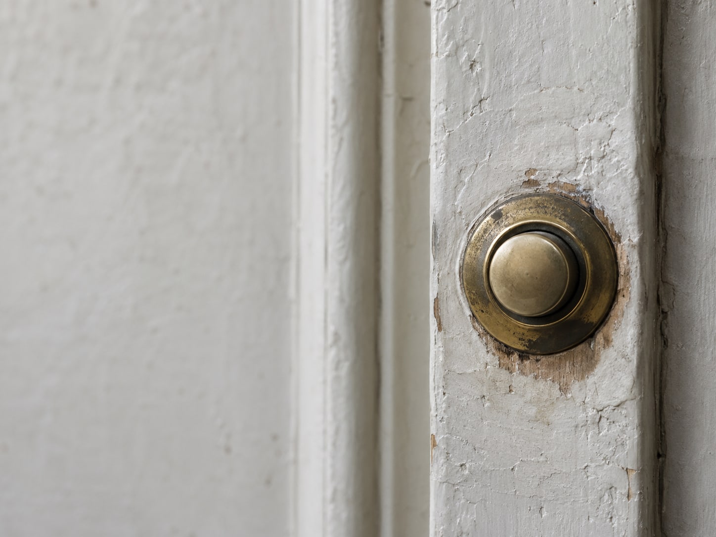 A worn brass doorbell button on a painted wooden door frame, the paint around it slightly rubbed away.