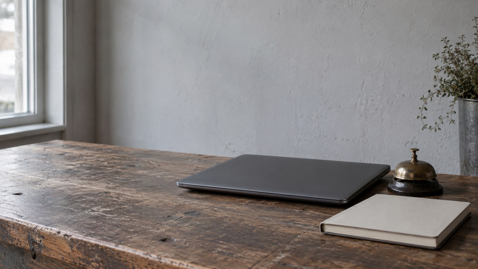 A closed laptop, a small brass bell and a blank appointment book arranged on a wooden shop counter.