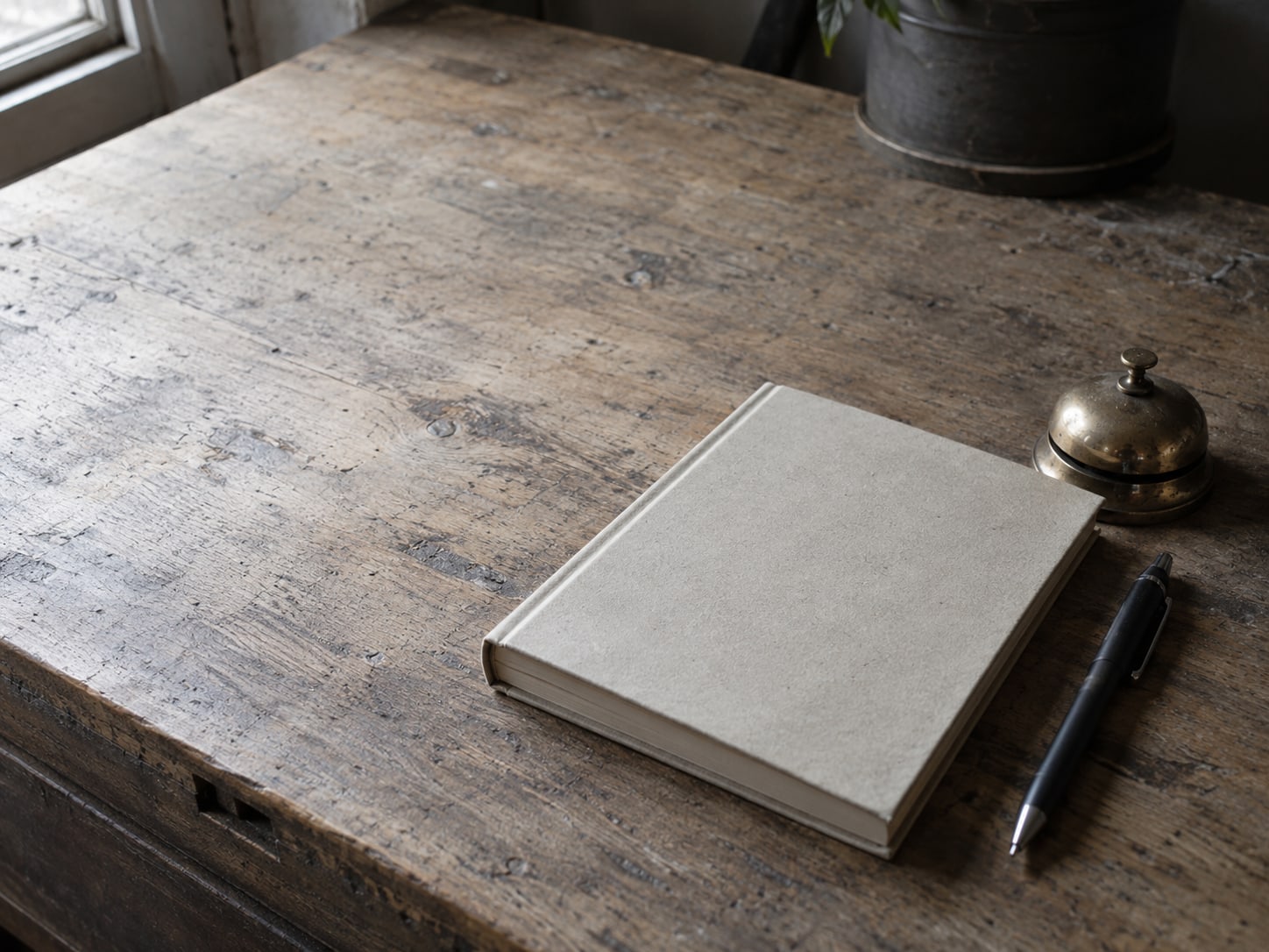 A paper appointment book lying closed beside a pen and a small brass bell on a shop counter.