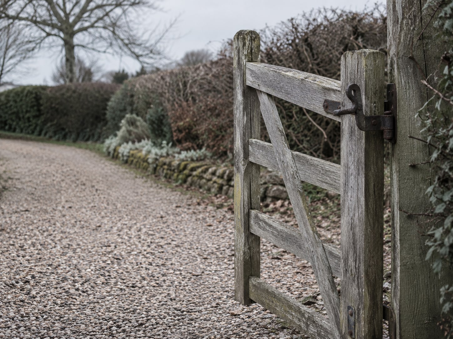 An old wooden garden gate standing open with its iron latch lifted, on a gravel path.
