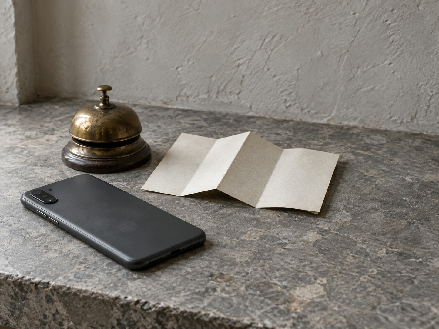 Un teléfono boca abajo sobre un mostrador de piedra junto a un mapa de papel doblado y un timbre de latón.