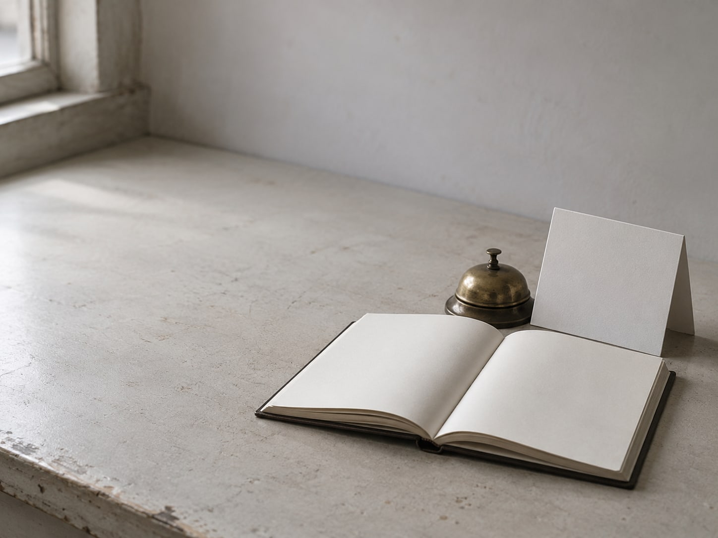 An open appointment book beside a blank folded paper calendar and a brass desk bell on a counter.