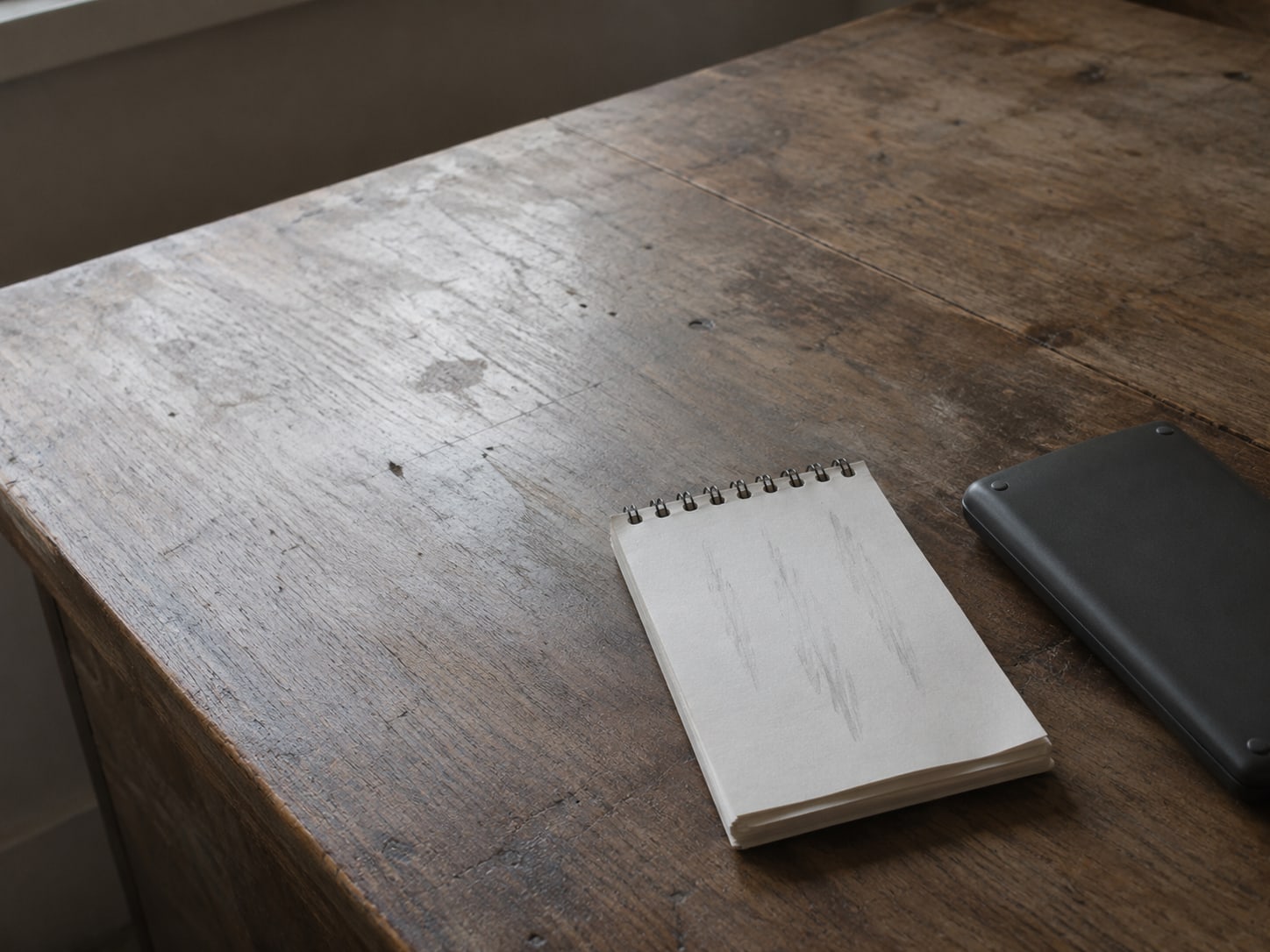 A small notepad with pencil marks in neat columns beside a flat calculator, switched off, on a plain table.