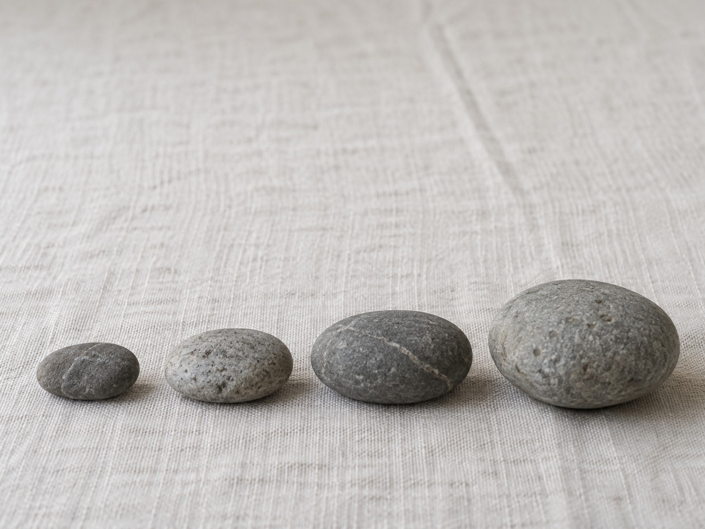 Una hilera ordenada de cuatro piedras lisas de tamaño creciente alineadas sobre un mantel de lino claro.