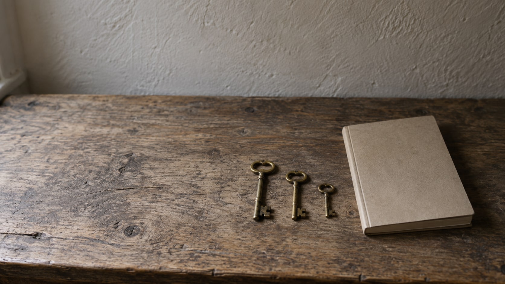 A row of three small brass keys of different sizes laid on a worn wooden counter beside a closed notebook.
