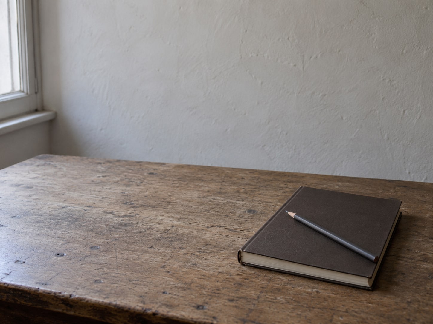 A closed ledger with a single pencil resting across it on an empty desk.