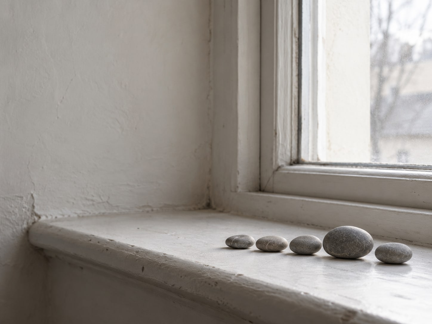 A neat row of small stones on a windowsill in morning light, one slightly larger than the rest.