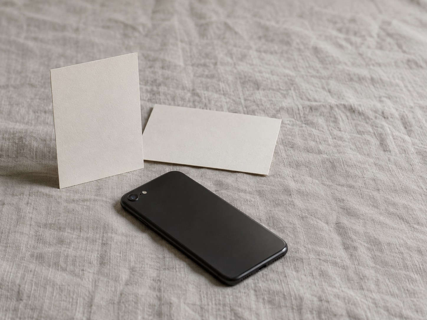 Two blank index cards, one placed upright and one placed sideways, next to a closed phone lying face down on a linen cloth.