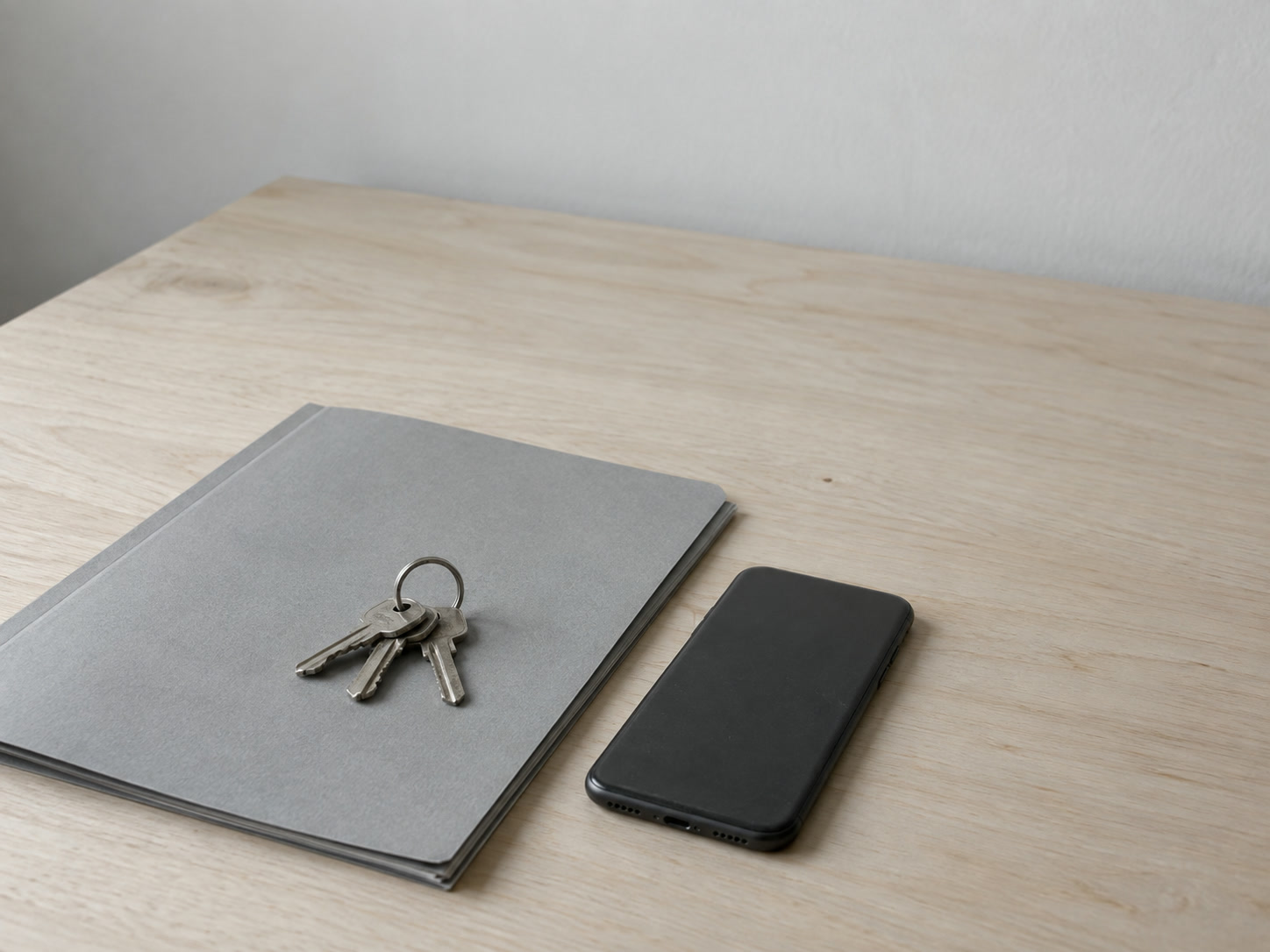 A small ring of keys resting on a closed folder on a clean desk, with a switched-off phone lying face down beside it.