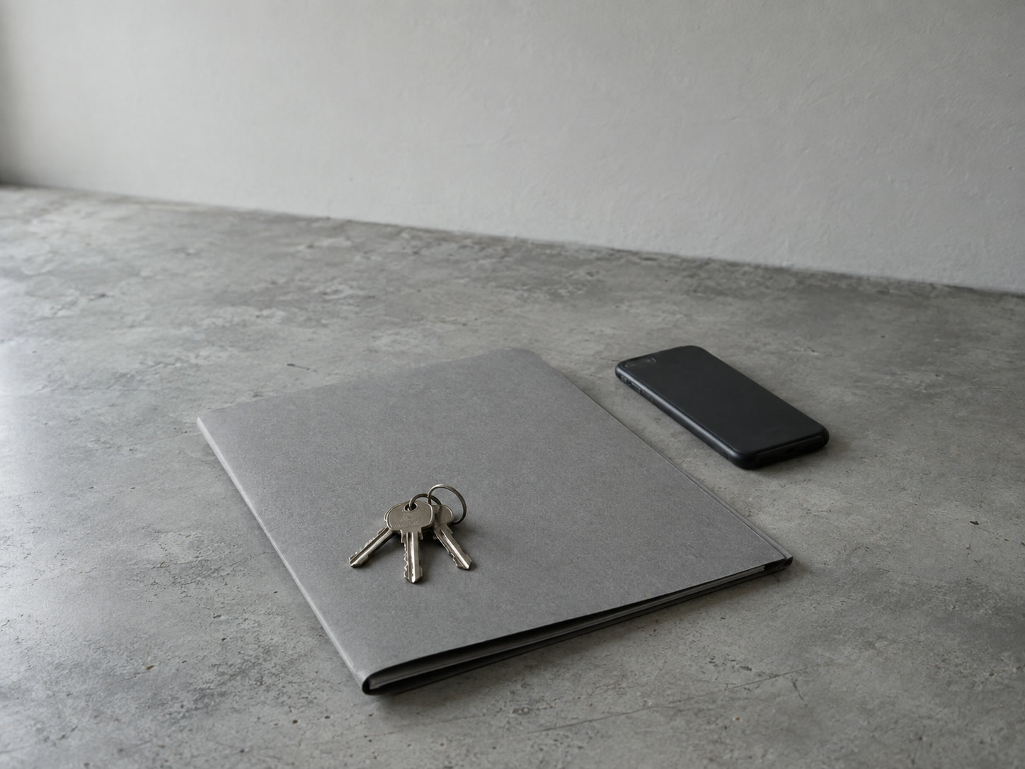A ring of keys resting on a closed blank folder on a gray desk, with a switched-off phone lying face down nearby.