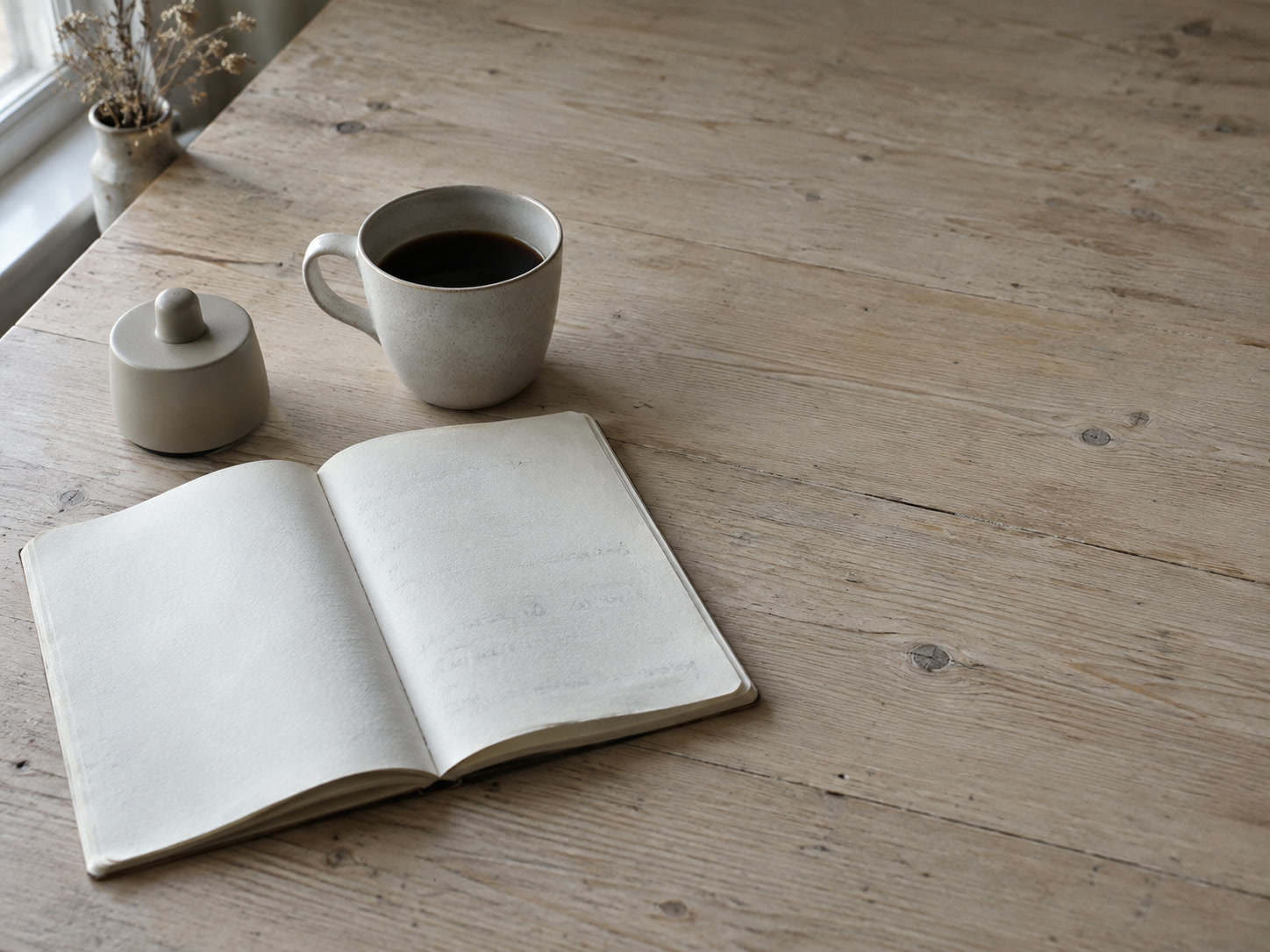 An open notebook with faint unreadable pencil marks beside a kitchen timer and a cup of coffee on a wooden table.