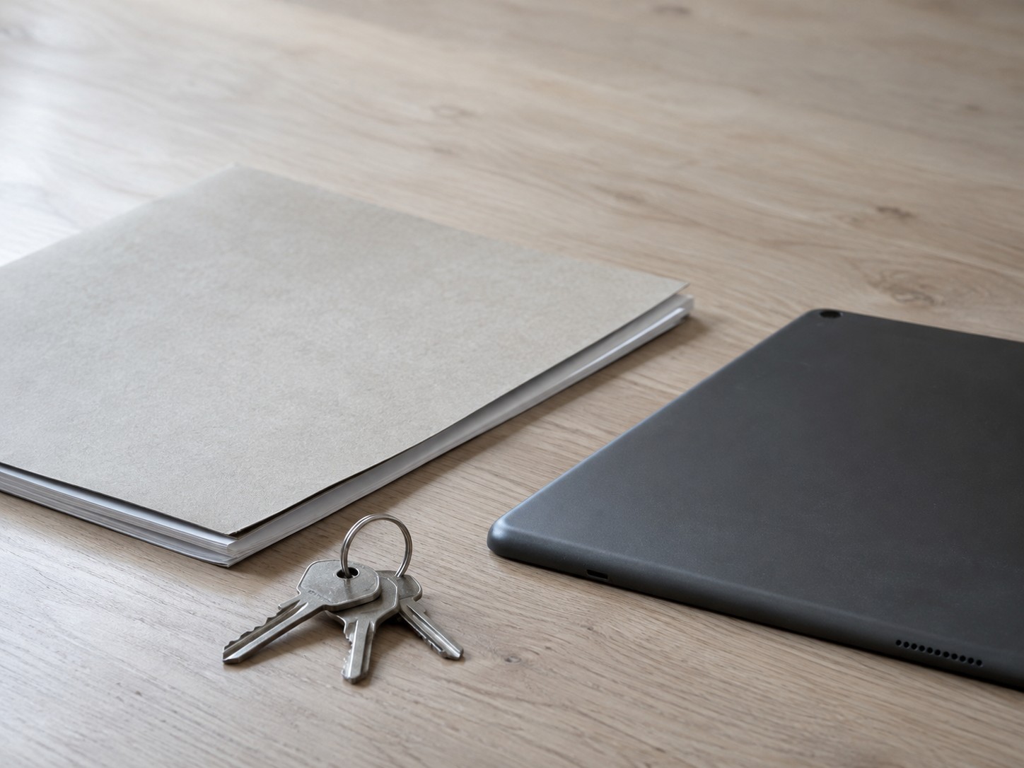 A small ring of keys and a closed folder of blank pages resting on a clean desk beside a switched-off tablet lying face down.