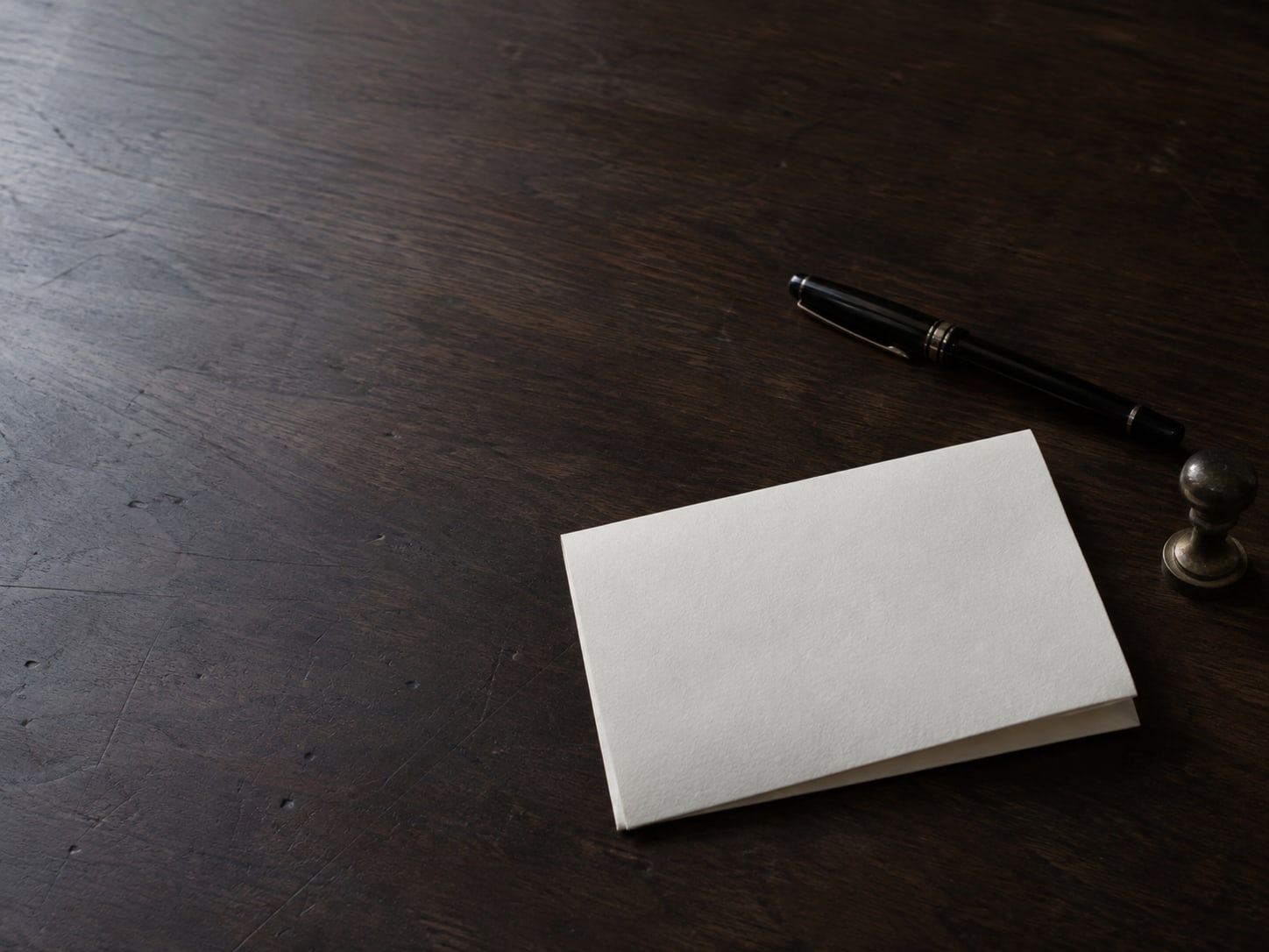 A folded blank letter beside a closed fountain pen and a small wax seal stamp on a dark walnut desk.