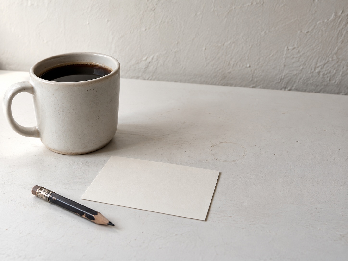 A short pencil, a blank index card and a cup of coffee on a clean white table.