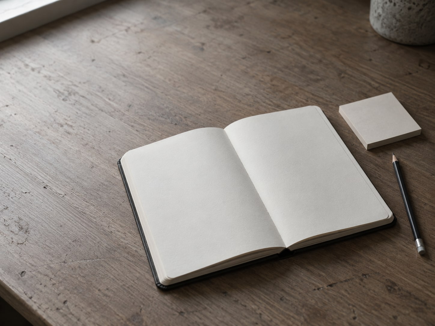 A paper planner lying open beside a pencil and a small stack of blank sticky notes on a desk.