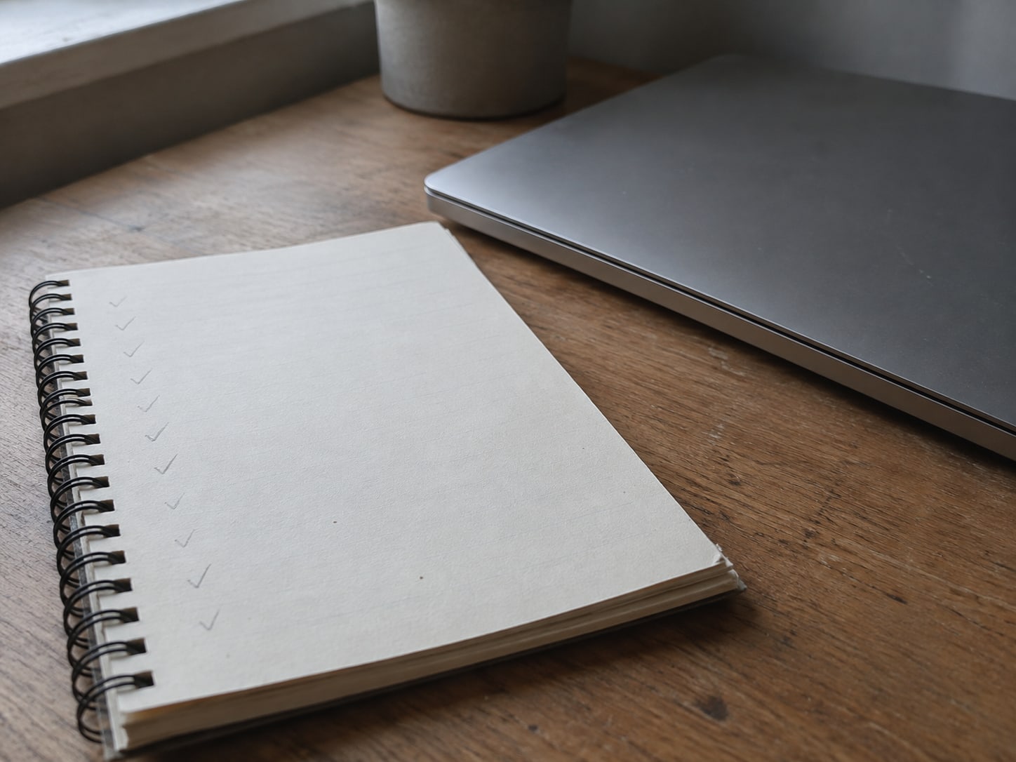 A blank notepad with faint pencil ticks down the margin, resting beside a closed laptop on a wooden desk.