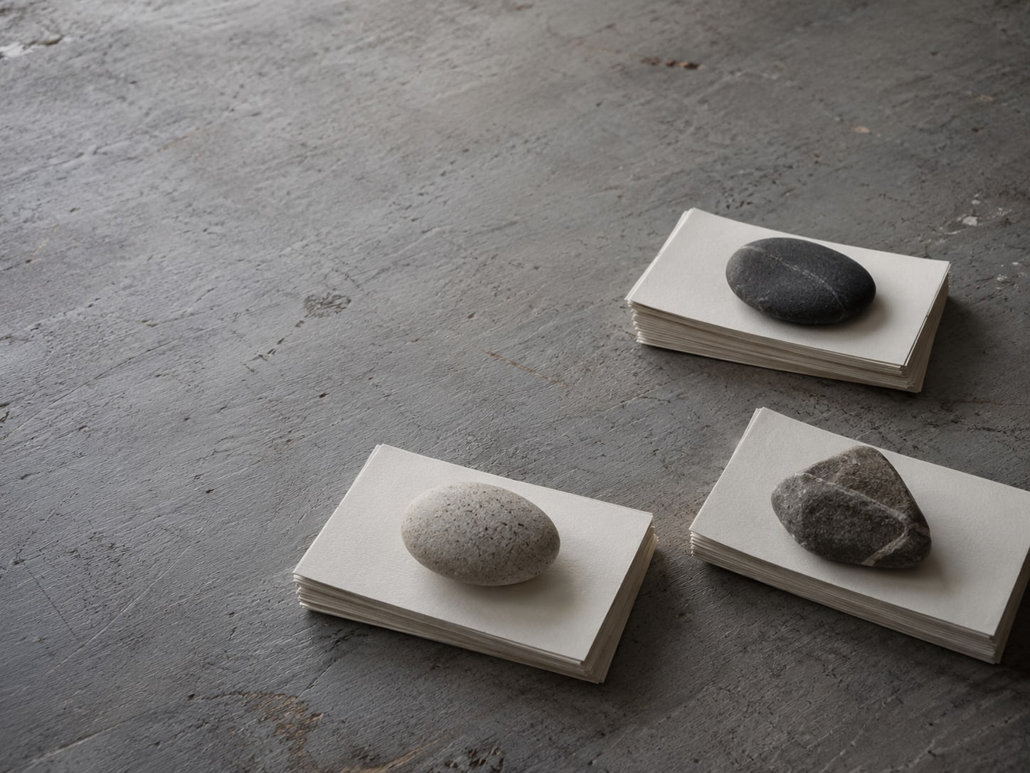 Three small stacks of blank index cards on a desk, each stack held down by a different smooth stone.
