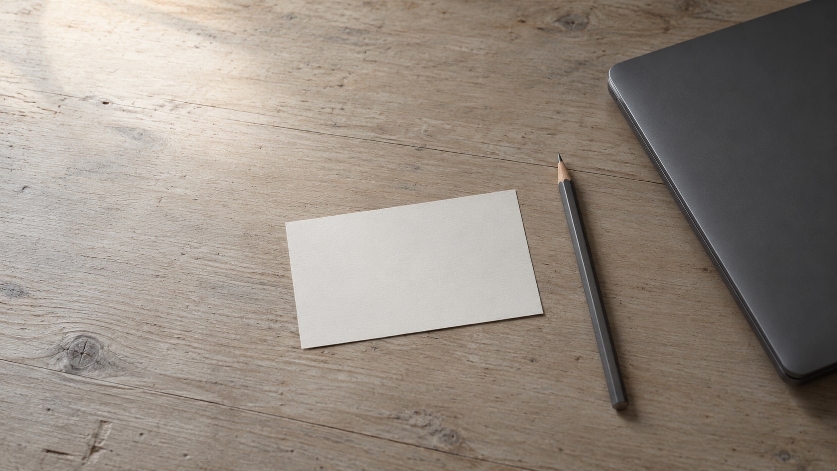 A single blank index card centered on a clean wooden desk beside a sharpened pencil and a closed laptop.