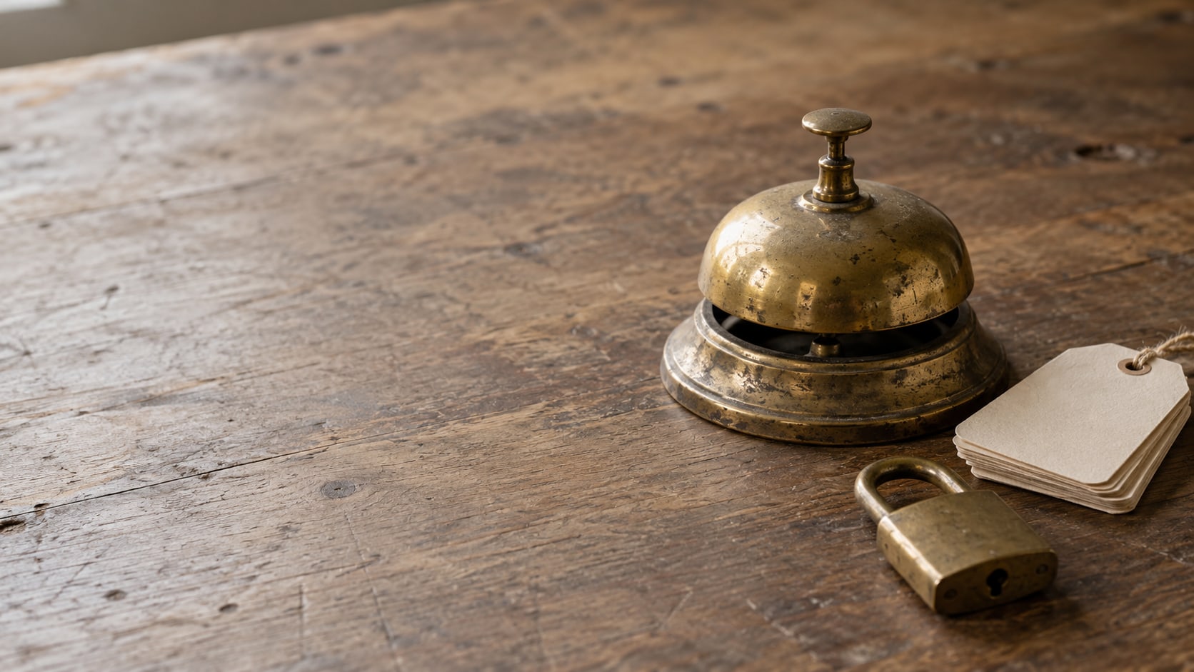 A single brass desk bell on a wooden counter beside a small stack of blank paper tags and a closed padlock.