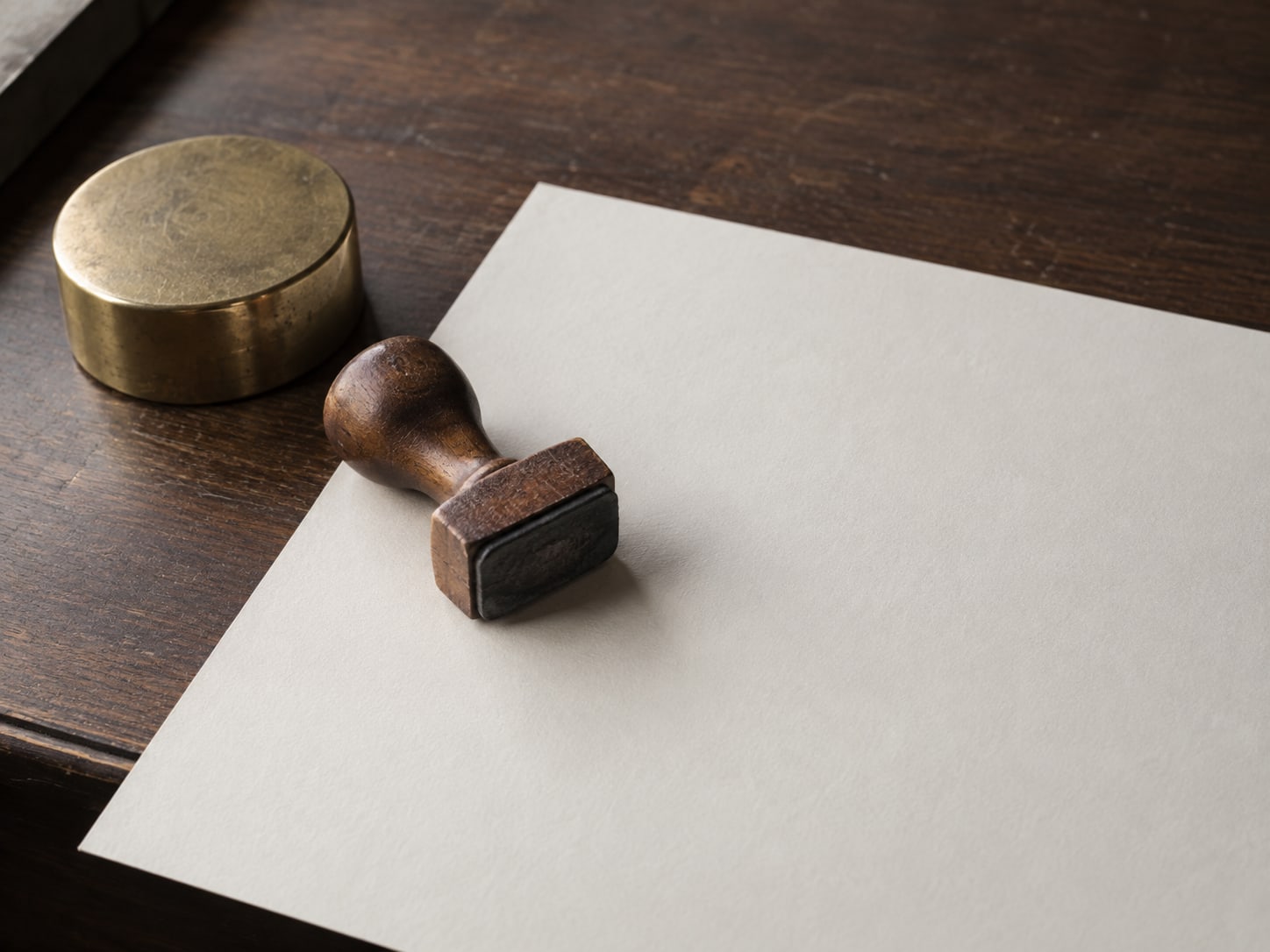 A small wooden rubber stamp resting on a blank sheet of cream paper beside a brass paperweight on a dark walnut desk.
