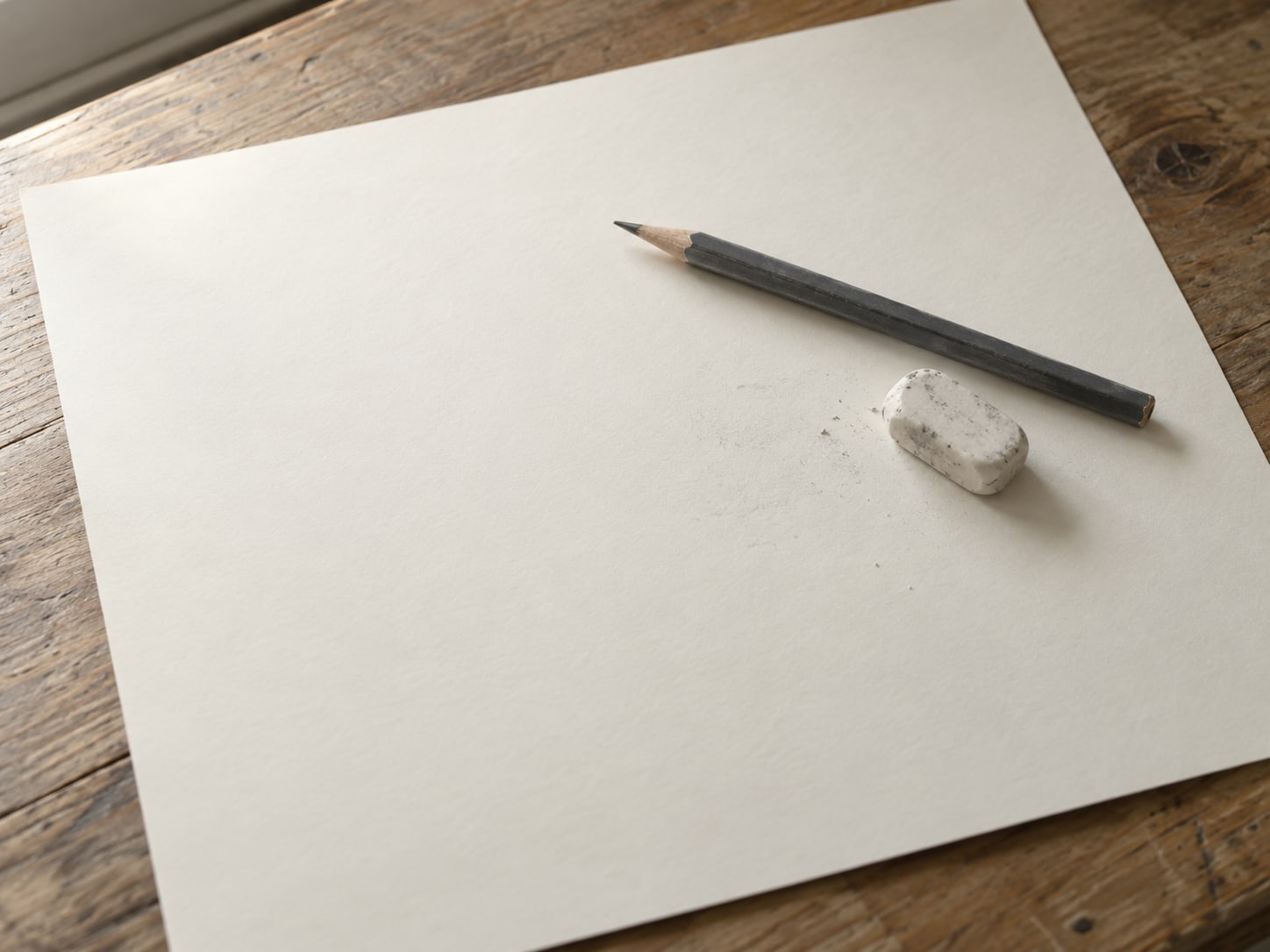 A pencil and an eraser resting on a sheet of blank paper with a few faint unreadable pencil marks.
