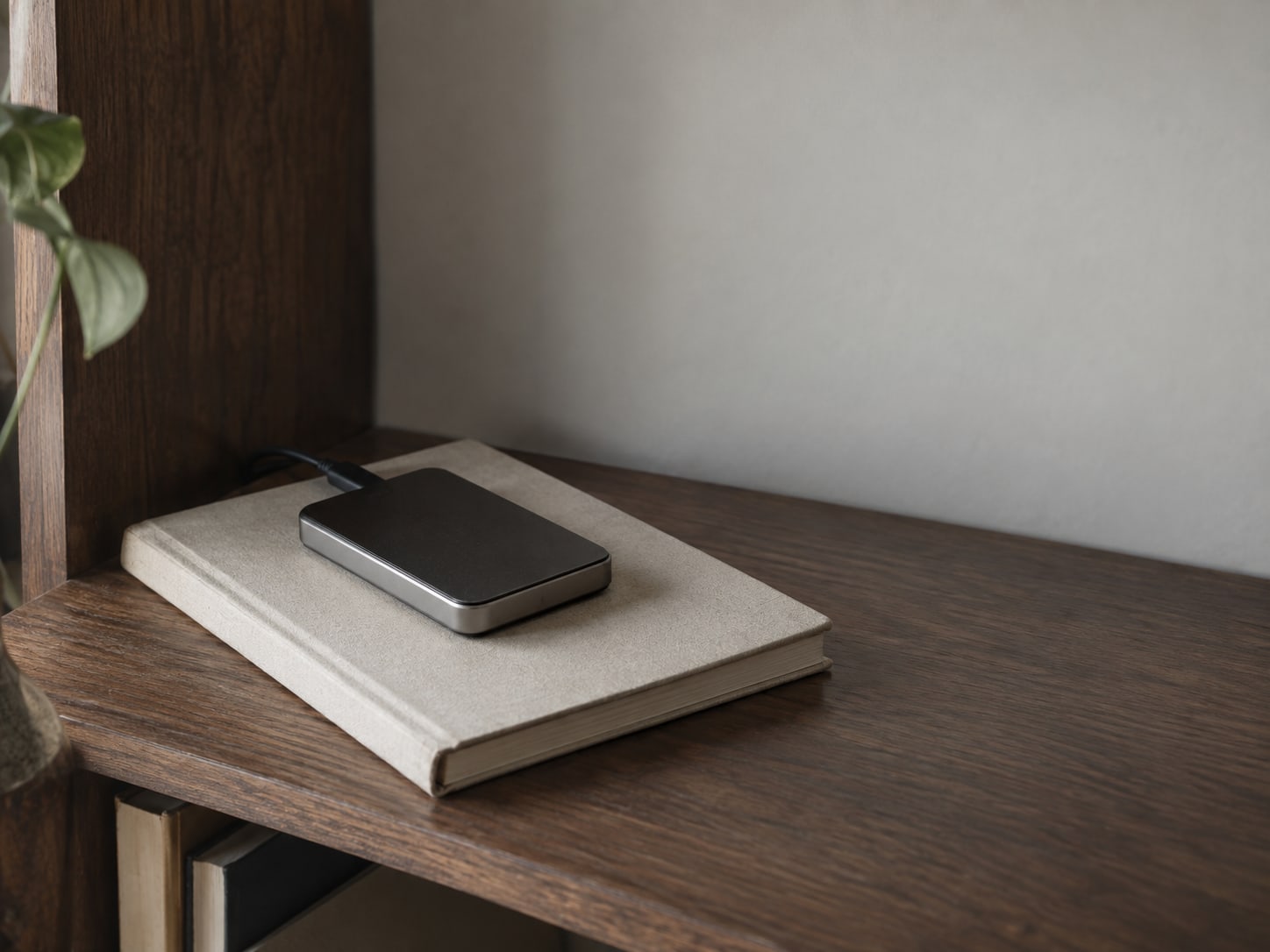 A small external hard drive resting on a closed paper address book on a walnut bookshelf.