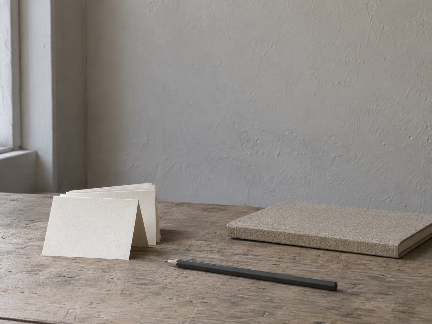 A small stack of folded price cards and a pencil on a tidy shop counter beside a closed appointment book.