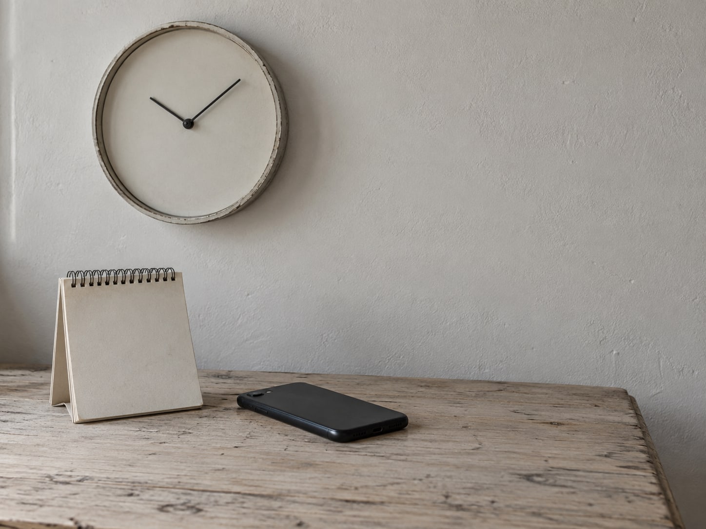 A wall clock and a small desk calendar with a few unreadable pencil marks, set beside a closed phone lying face down.