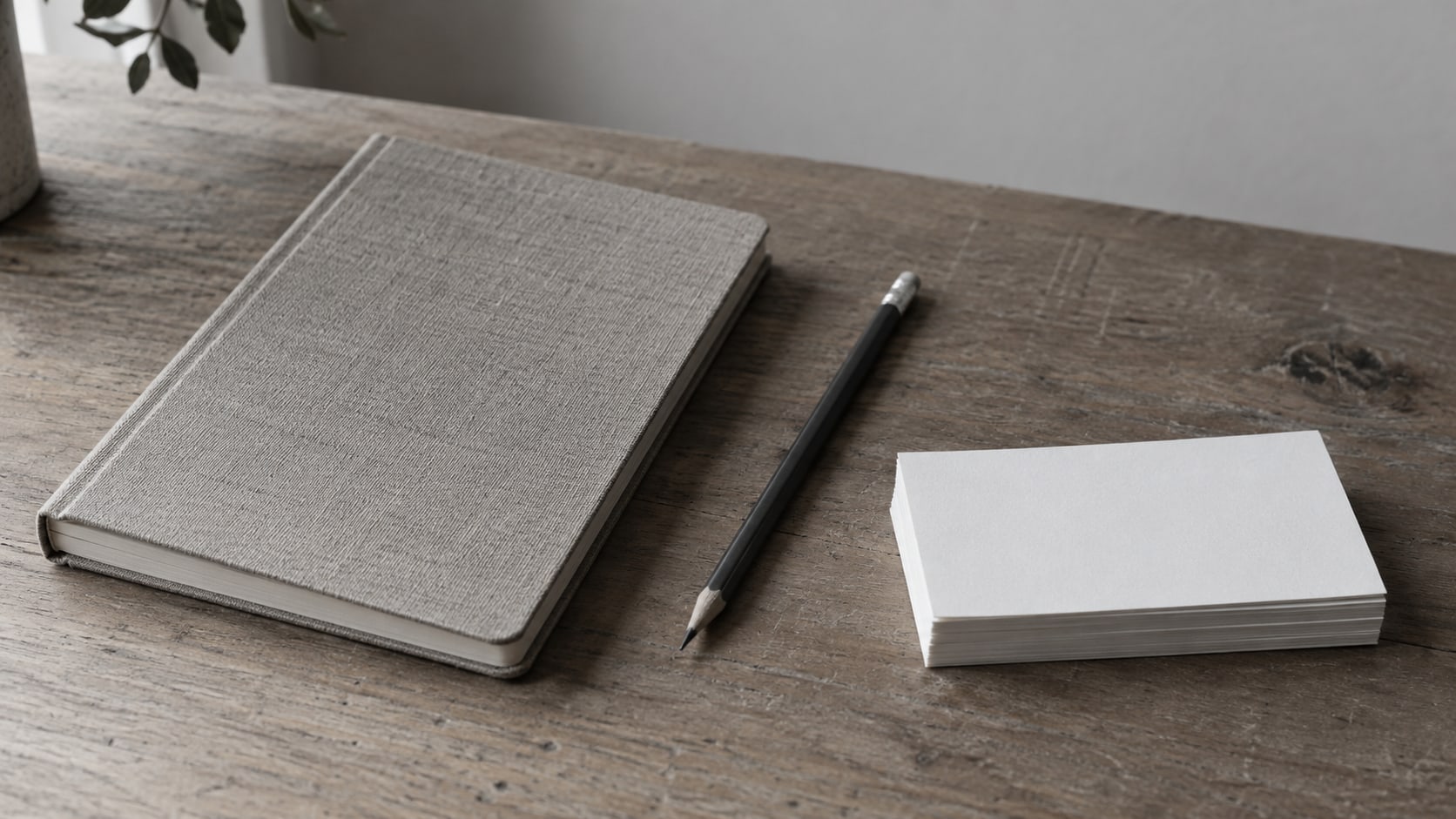 Un cuaderno cerrado y un lápiz sobre un escritorio de madera junto a una pequeña pila de fichas en blanco.